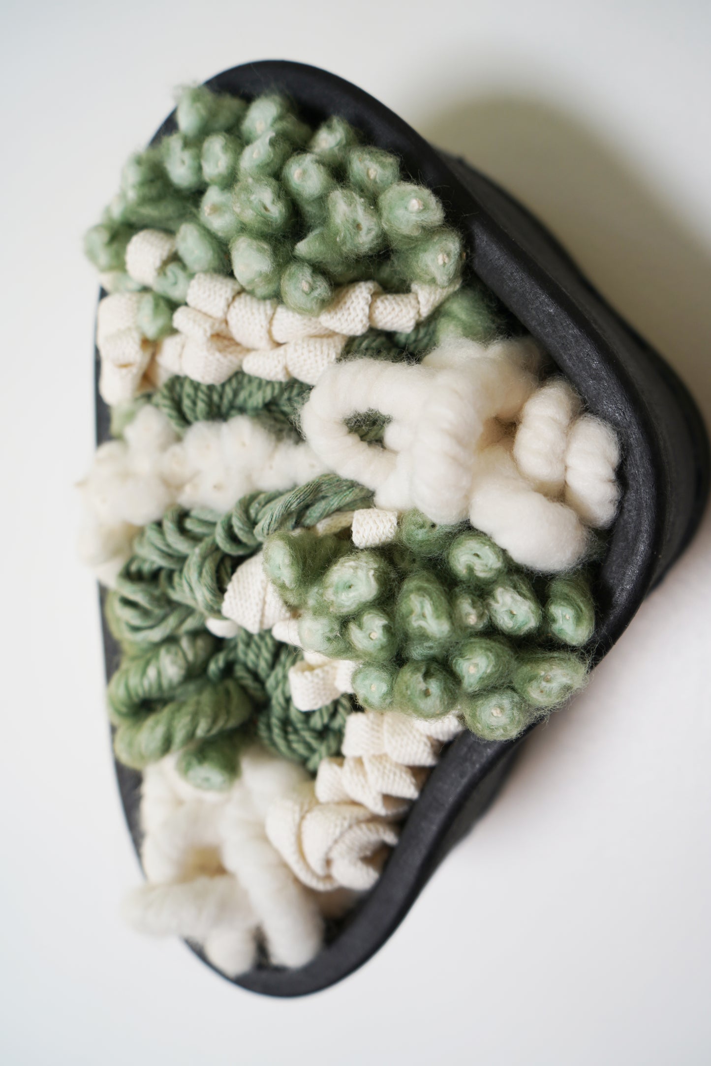 Modern sculptural wall hanging displayed on a white wall to show scale. The 11-inch by 6.75-inch black clay frame serves as a striking focal point, perfect for entryways or gallery walls seeking organic, botanical-inspired decor.