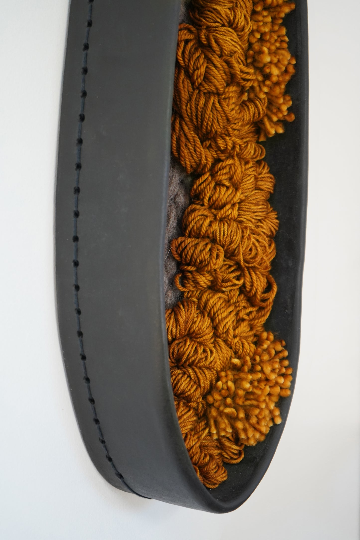Side profile of black clay wall frame revealing 3.5 inch depth. Oval ceramic bottom filled with grey and deep orange and mustard yellow wool loops.