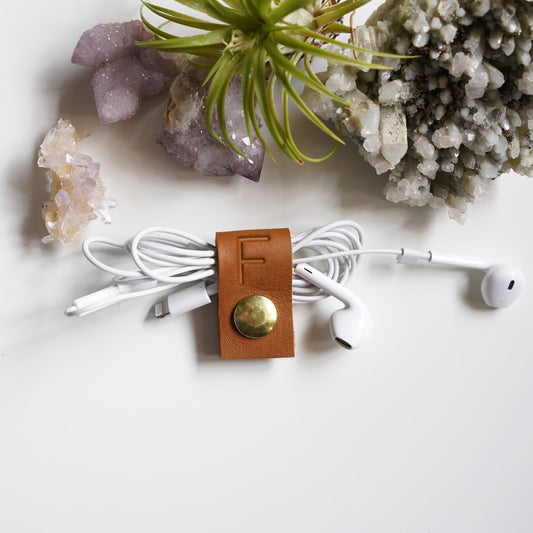 Personalized brown leather earbud cord organizer with custom F initial, handmade headphone cable holder with brass snap for tangle-free earbud storage, travel and everyday tech organization by Keyaiira
