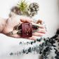 Wine leather cable keeper with personalized M initial securing a braided charging cord, carefully crafted by Keyaiira for USB cables, mobile electronics, travel tech and cable management
