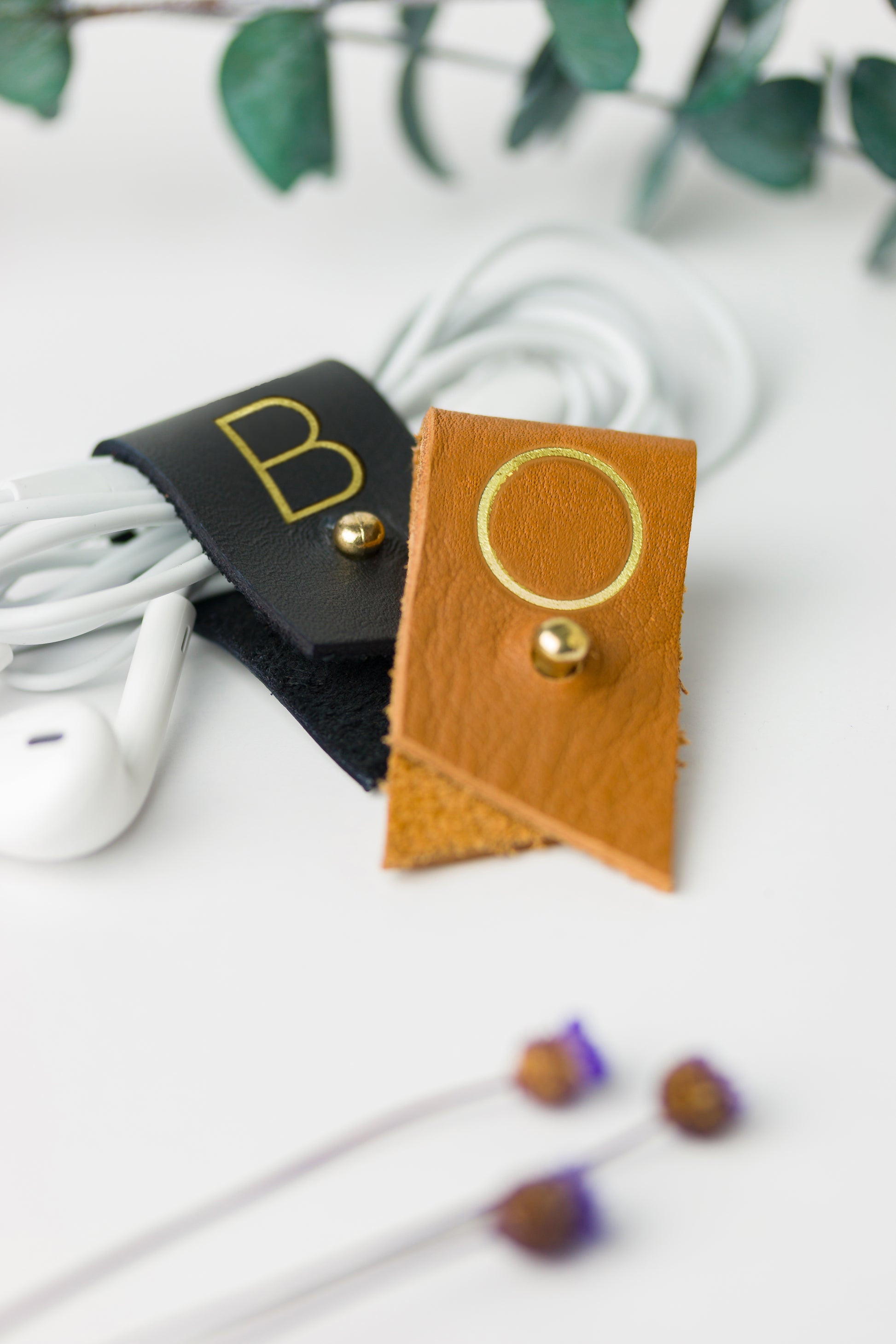 Black and warm golden leather cord organizers with customized B and O letters, individually crafted by Keyaiira for headphones, phone chargers, device cords and portable tech storage
