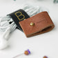 Black and Chocolate full-grain leather cable holders with custom initial detailing, handmade by Keyaiira for charger cables, computer cords, electronic accessories and organized workspace storage

