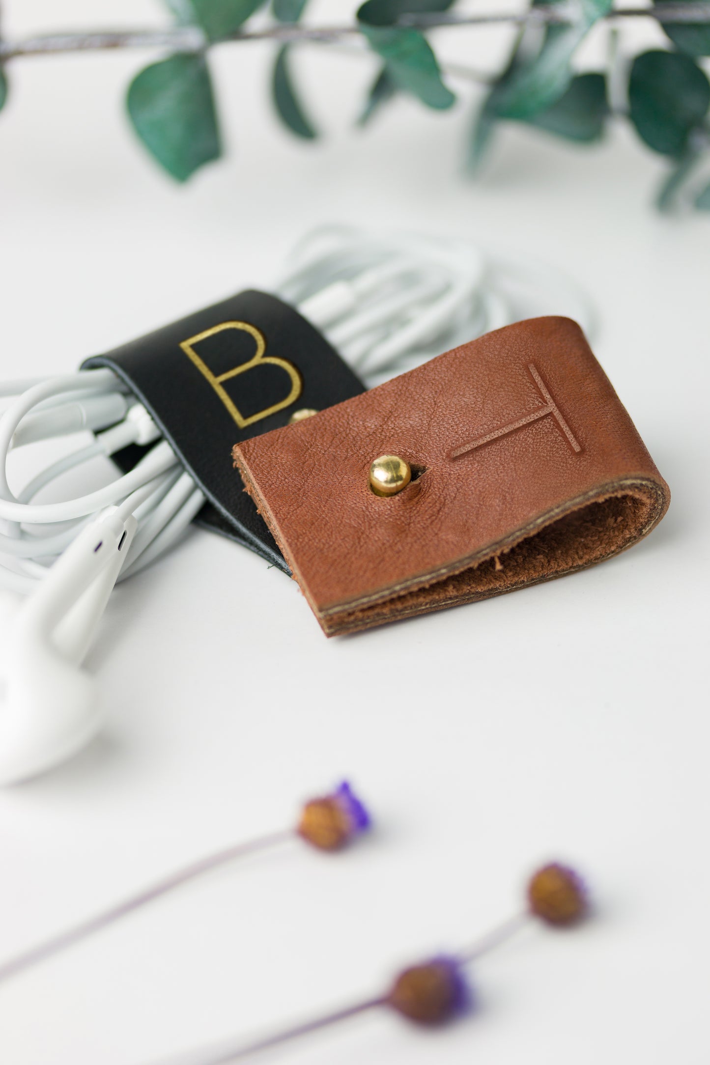 Black and Chocolate full-grain leather cable holders with custom initial detailing, handmade by Keyaiira for charger cables, computer cords, electronic accessories and organized workspace storage
