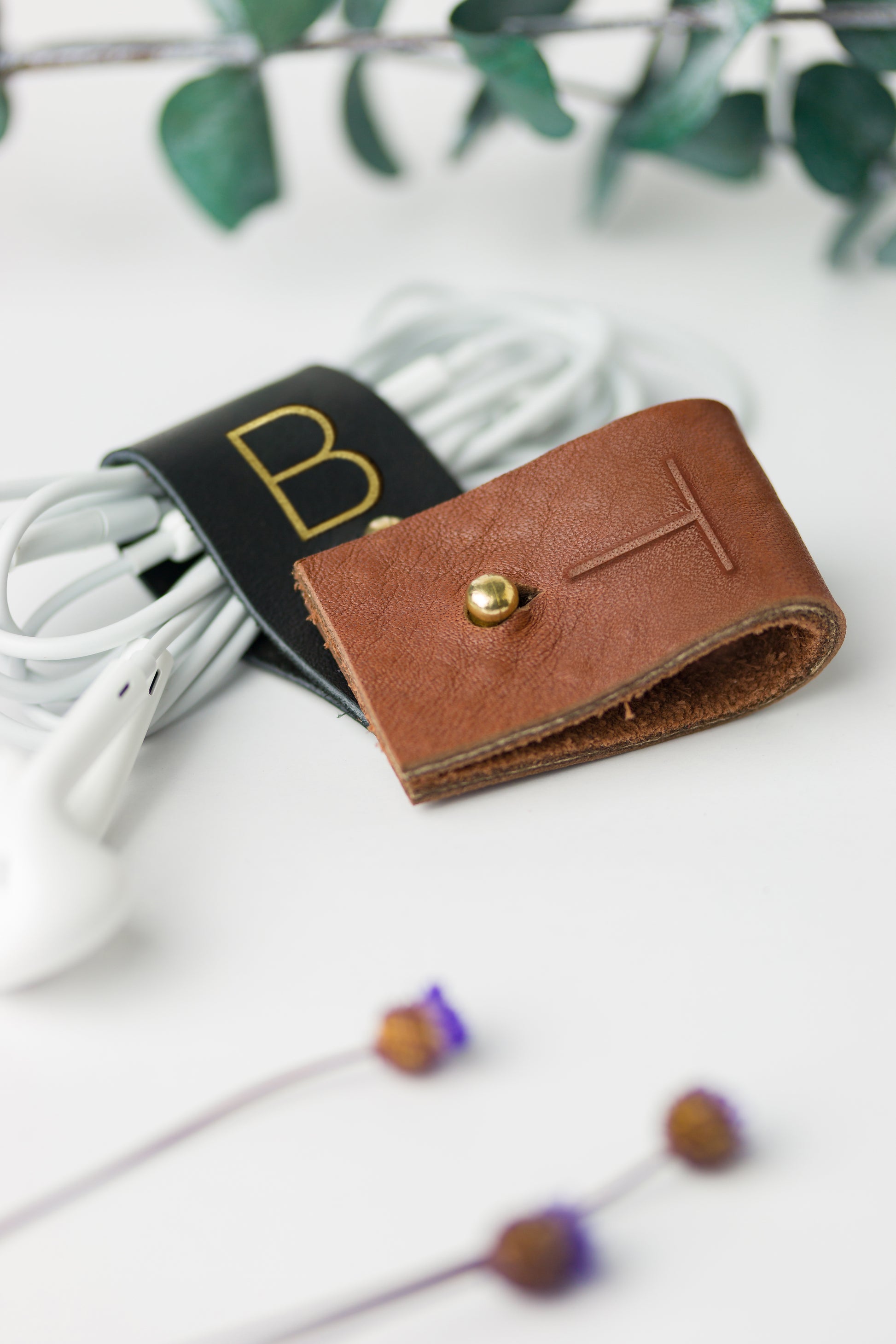 Black and Chocolate full-grain leather cable holders with custom initial detailing, handmade by Keyaiira for charger cables, computer cords, electronic accessories and organized workspace storage
