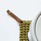 Detachable leather hanging loop attached to a knit potholder next to cookware — Keyaiira leather loop for kitchen organization.