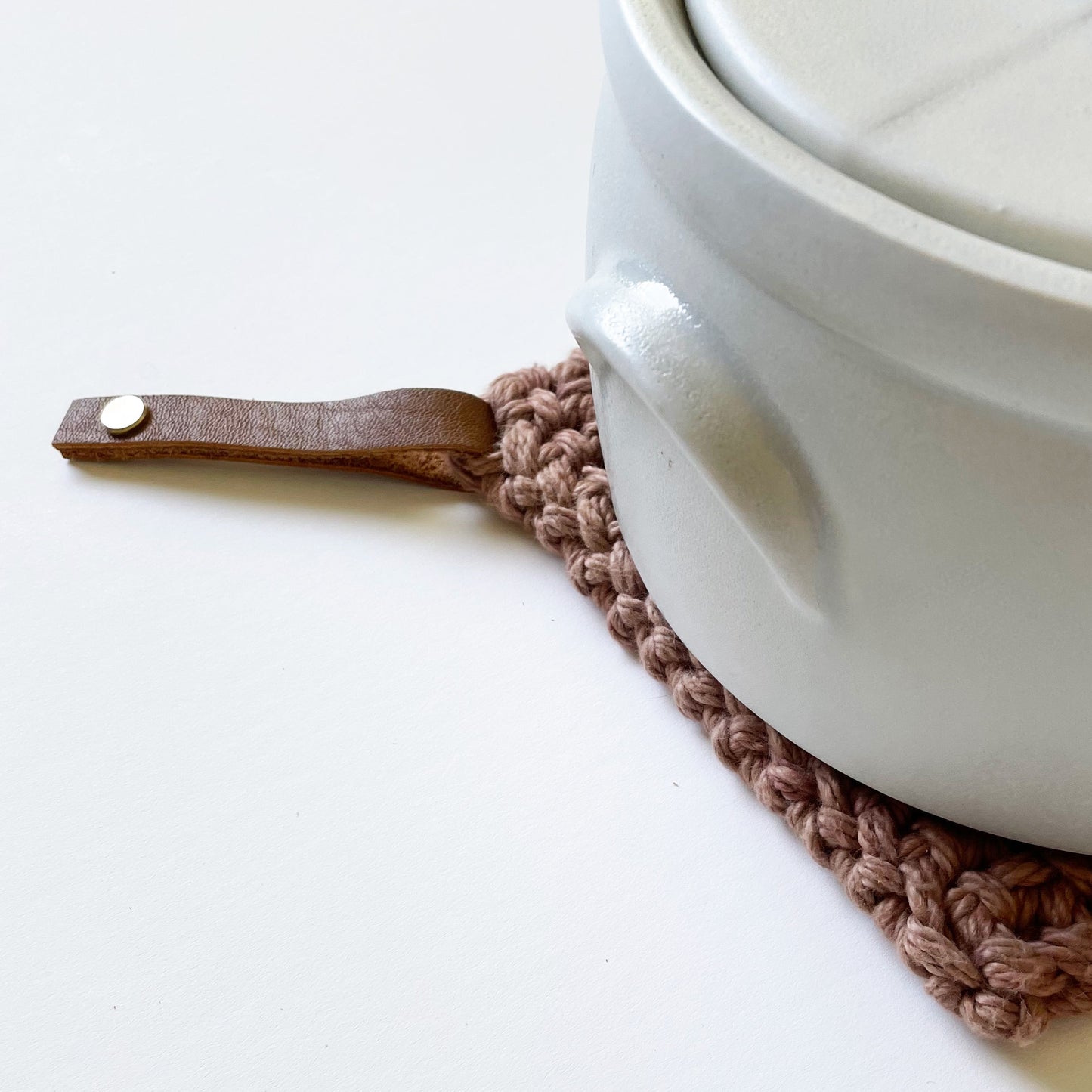 Close-up highlighting the detachable leather hanging loop on a knit potholder — Keyaiira removable leather loop detail.