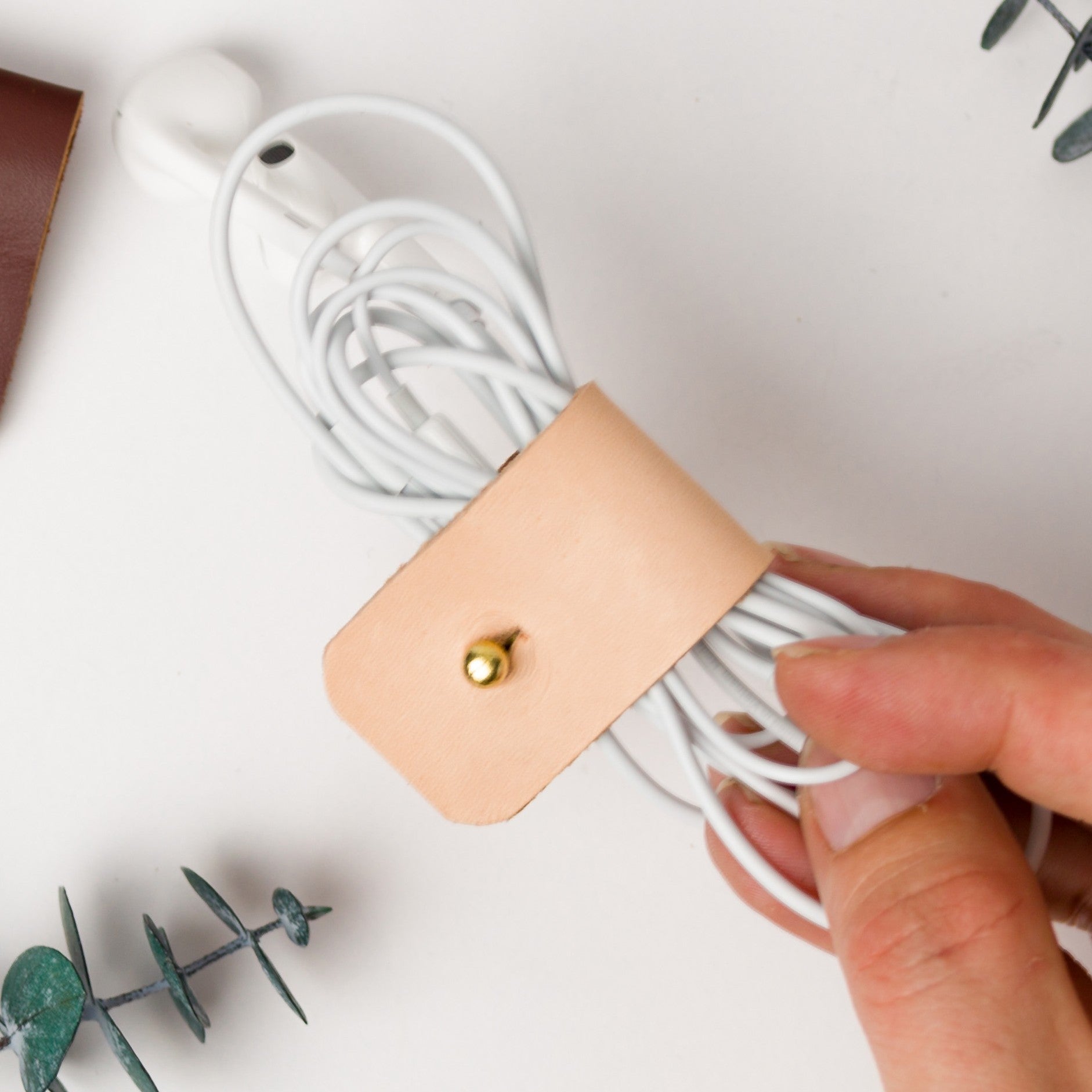 Veg Tan full-grain leather headphone cord holder featuring understated brass stud & post hardware, designed by Keyaiira to keep wired earbuds and small charging cords securely bundled
