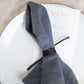 Leather Napkin Tie in black wrapped around a soft grey linen napkin with a printed menu card, minimalist, artisan-made table accessory crafted from sustainable leather for refined, modern dining decor by Keyaiira.