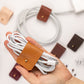 Handcrafted Cognac leather cable wrap securing a coiled white charging cord, reusable large cord organizer with Stud & Post hardware for desk, home office and travel organization by Keyaiira
