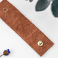 Rich brown full-grain leather cable wrap, carefully finished by Keyaiira with brass stud & post hardware for securing earbuds, charging cords and frequently used electronic cables
