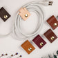 Black genuine leather cord keeper with double brass snap closures, minimalist cable management strap for charging cords, USB cables, headphones and home office electronics by Keyaiira
