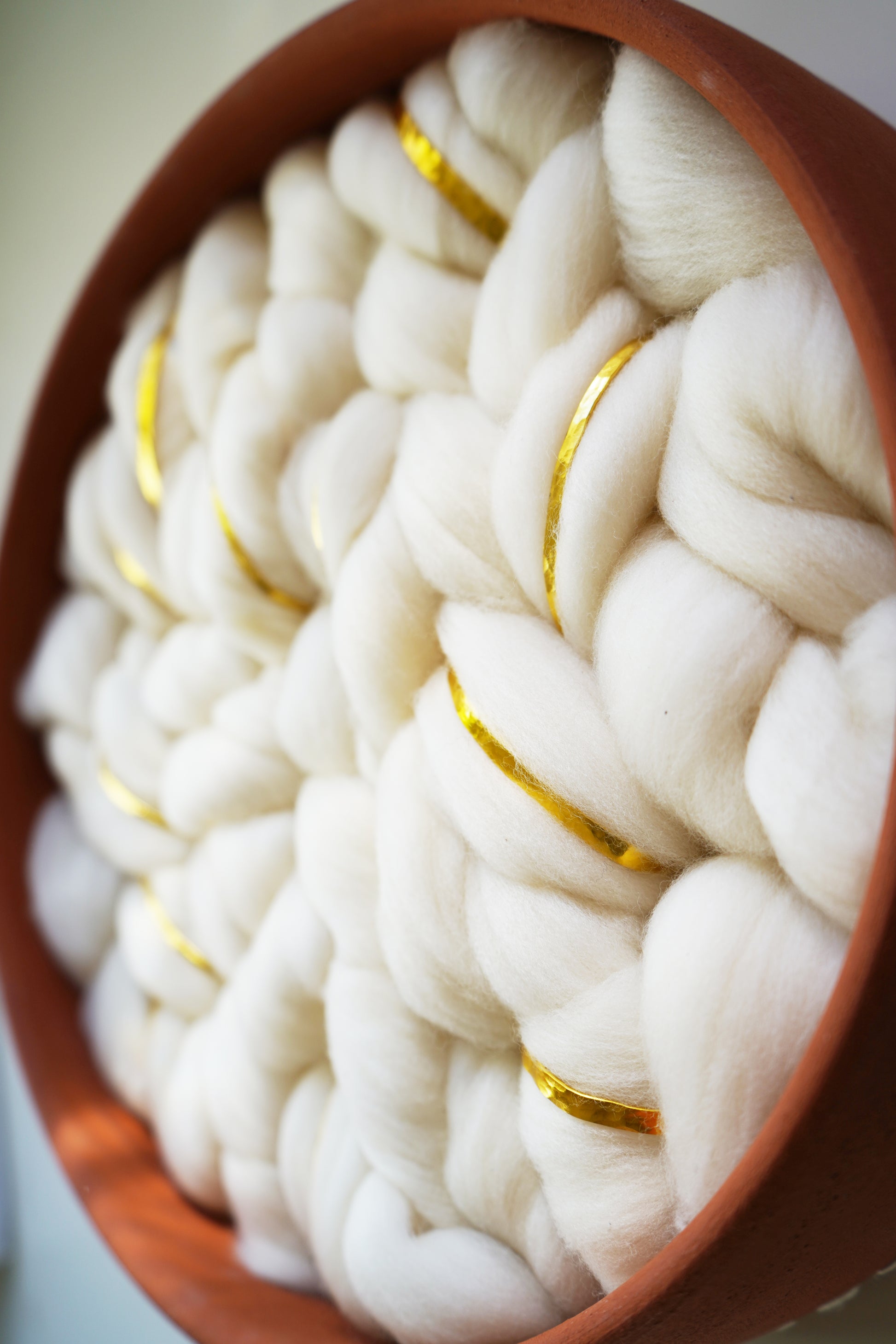 Close-up of un-dyed white Rambouillet wool roving showing the natural crimp and softness. The raw fiber texture contrasts with the smooth, matte finish of the surrounding terracotta clay rim.