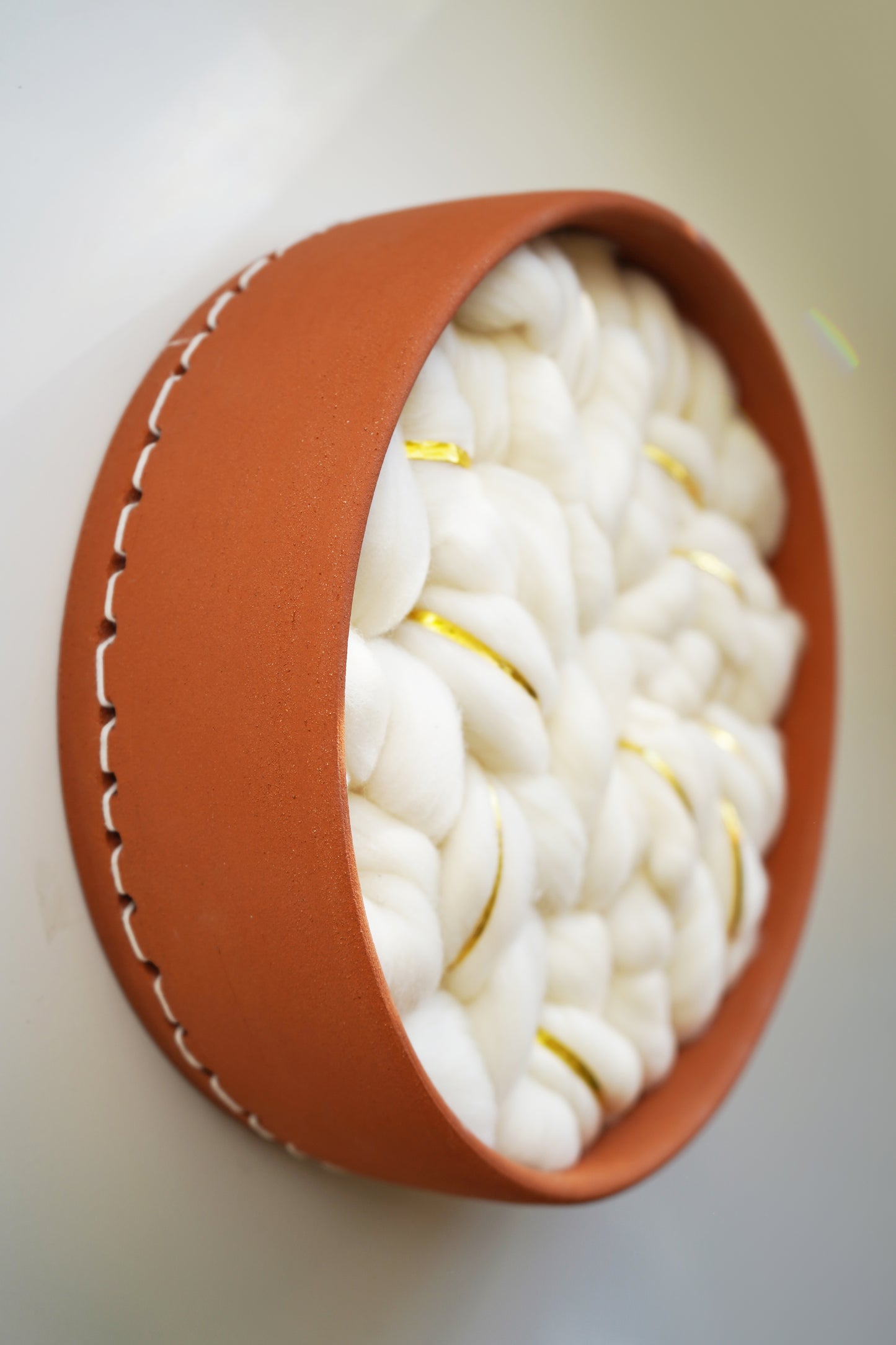 Angled view of the circular ceramic frame, hand-thrown in Sonoma, CA by artist Kala Stein. Highlights the contrast between the warm, hard clay and the soft, sustainable white wool interior.
