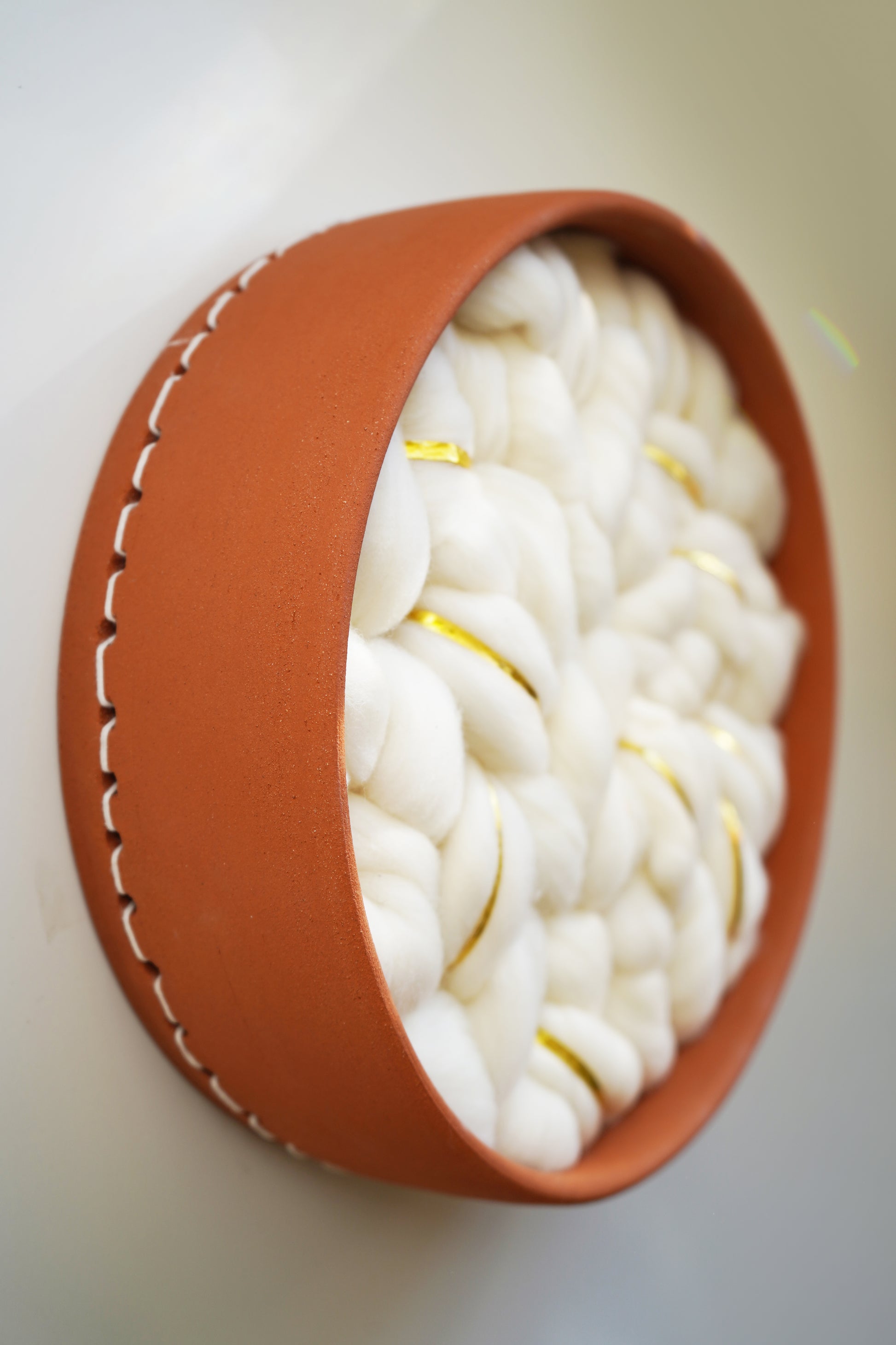 Angled view of the circular ceramic frame, hand-thrown in Sonoma, CA by artist Kala Stein. Highlights the contrast between the warm, hard clay and the soft, sustainable white wool interior.