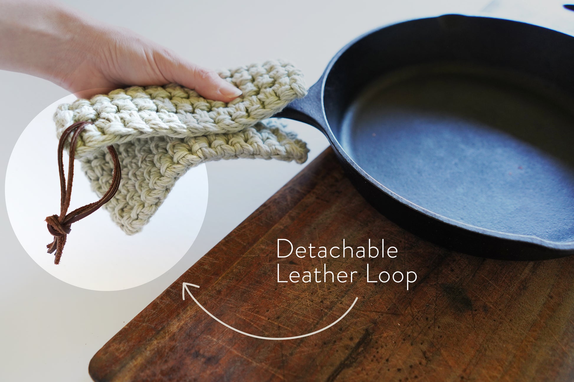 Detachable leather hanging strings by Keyaiira attached to a crocheted knit potholder and shown near cookware handcrafted leather hanging strings for organizing kitchen textiles.