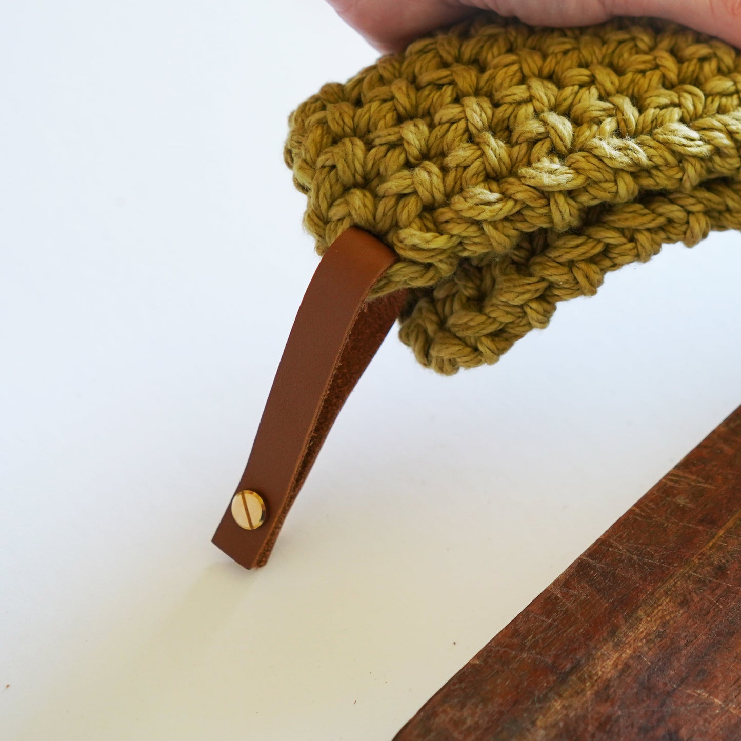 Leather hanging loop attached to a green knit potholder, shown hanging over a counter removable Keyaiira leather loop.