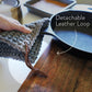 Person holding a blue-gray crocheted knit potholder with detachable leather hanging strings by Keyaiira over a wooden surface — removable leather hanging strings with brass hardware.