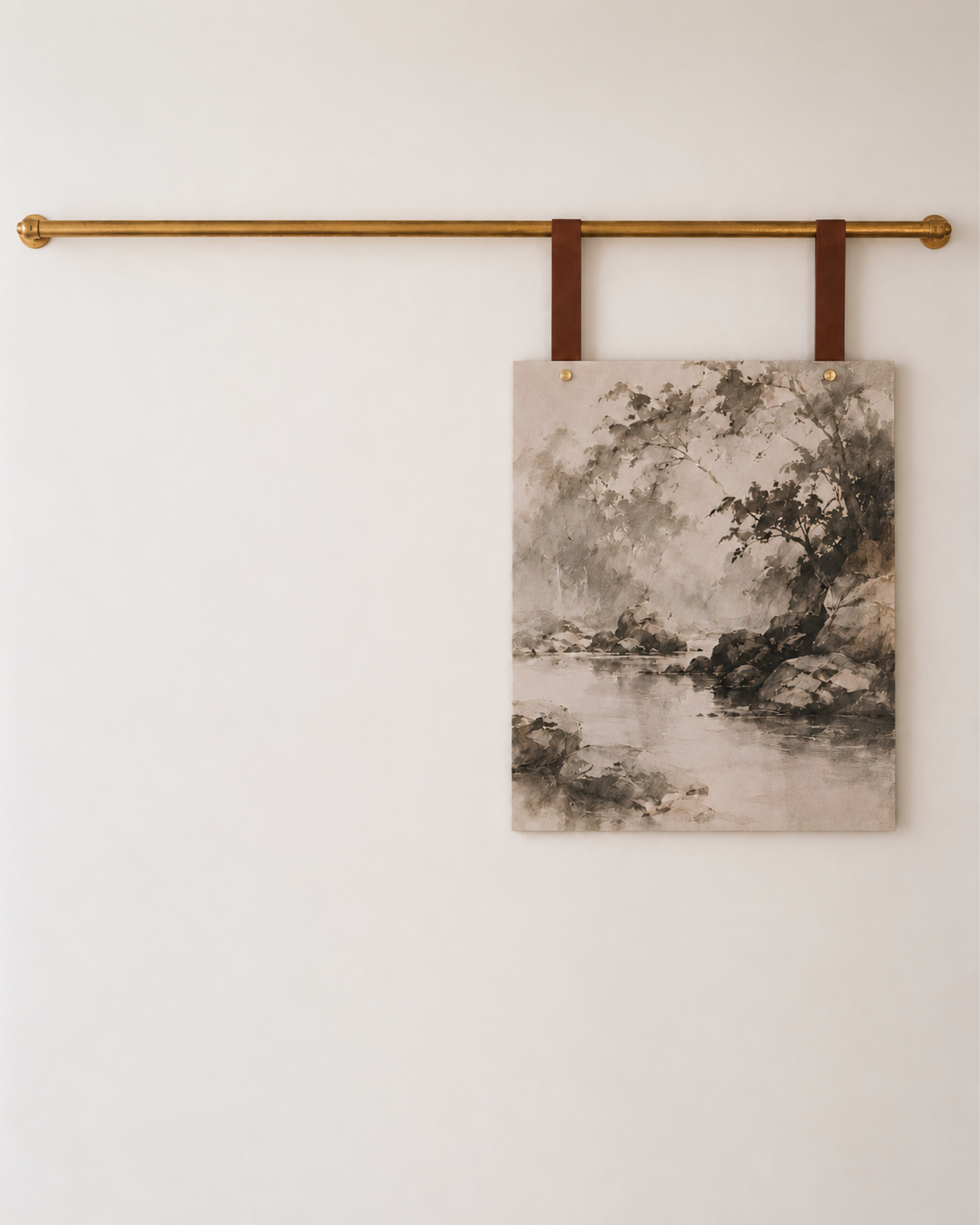 A rectangular wall art print with a sepia-toned landscape scene hangs from two brown leather straps on a gold horizontal rod against a plain off-white wall.