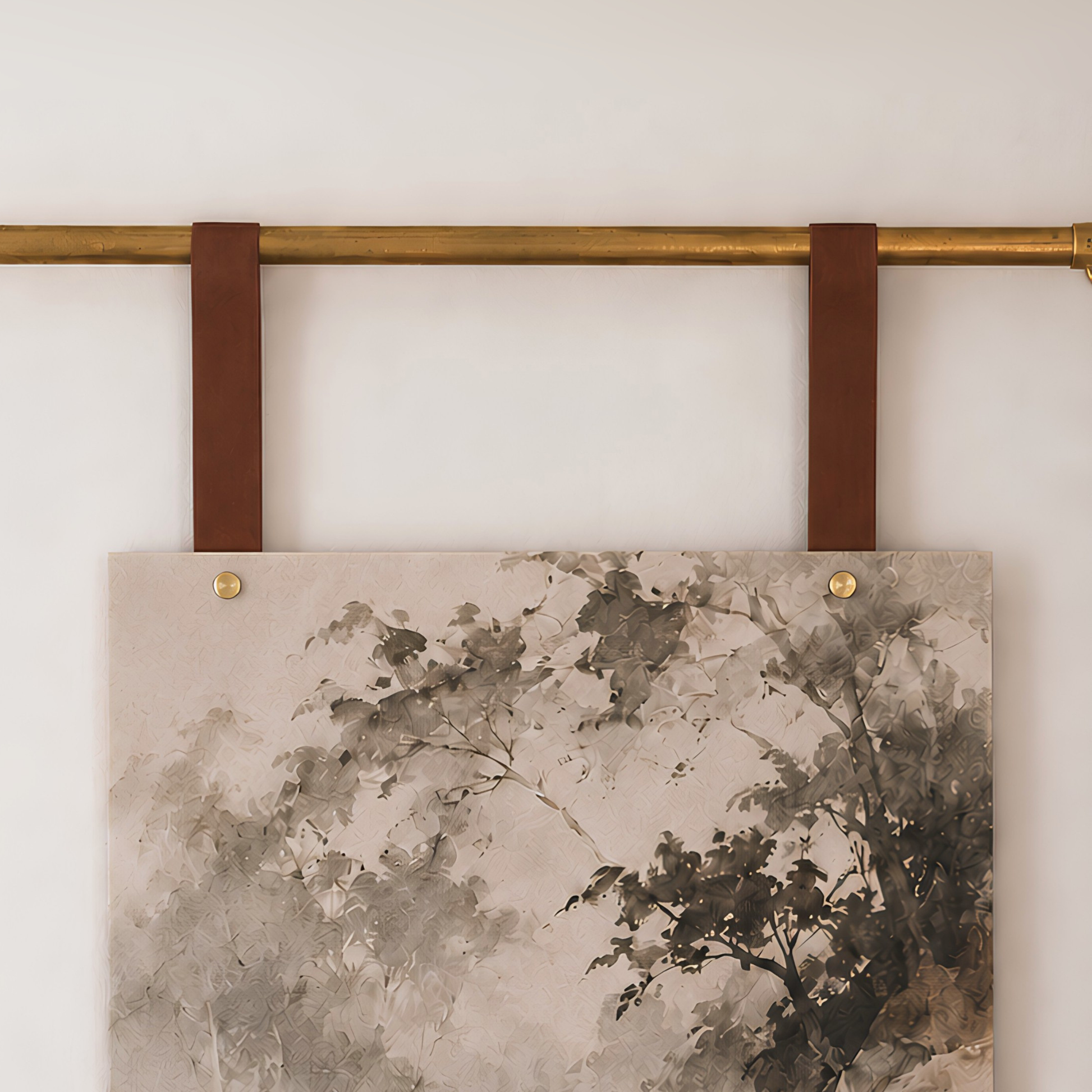 A square wall art print with an abstract tree design in muted gray, black, and beige tones, hanging from a brass rod with two leather straps against a white wall.