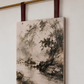 A vertical canvas wall art print featuring an ink-wash style landscape painting of trees and water, hanging from a brass rod with dark red leather straps against a plain white wall.