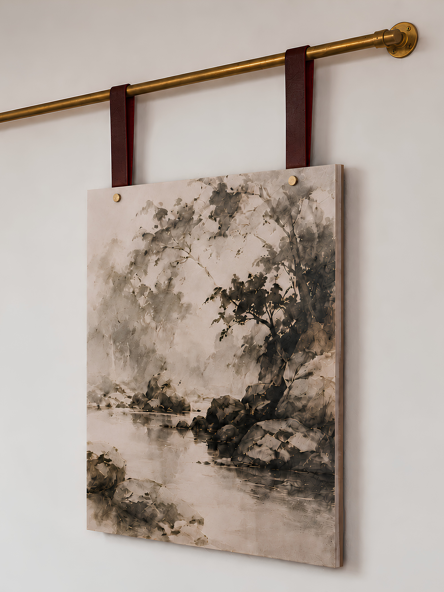 A vertical canvas wall art print featuring an ink-wash style landscape painting of trees and water, hanging from a brass rod with dark red leather straps against a plain white wall.