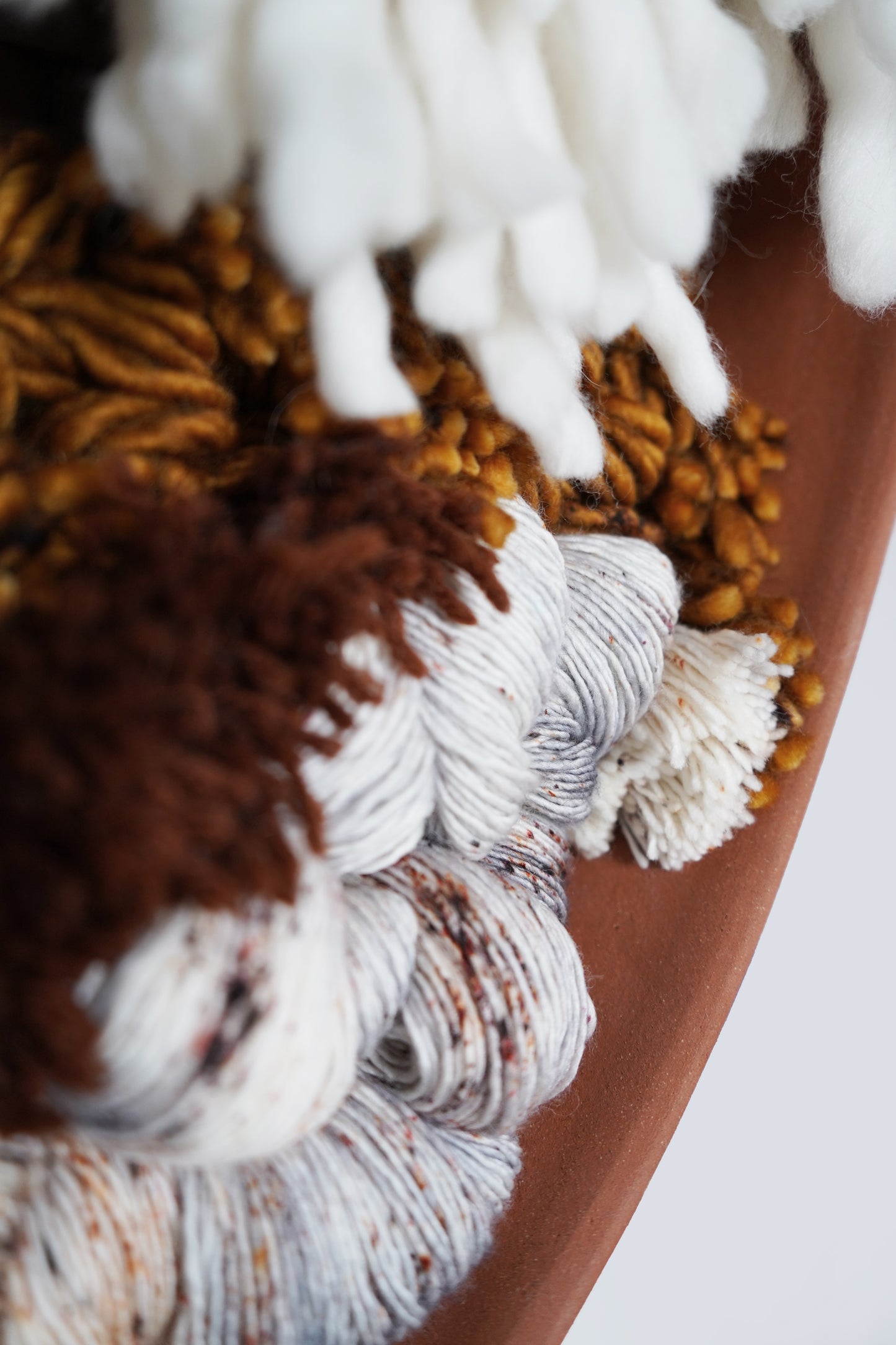 Close-up of hand-spun rust and gray wool fibers in terracotta frame.
