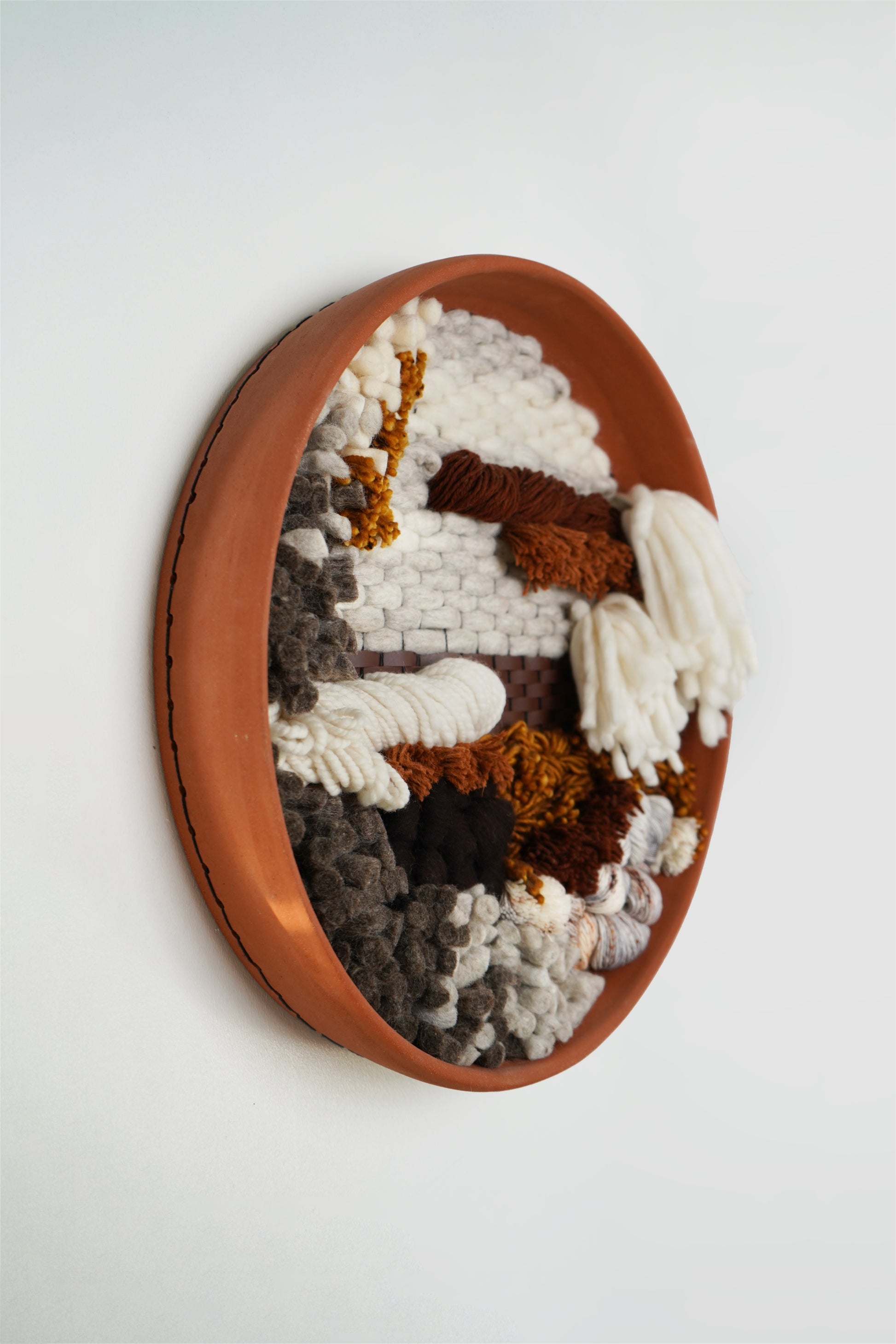 Side profile of clay wall art showing deep texture of woven fibers with earthy tones on a white wall, handmade by Keyaiira