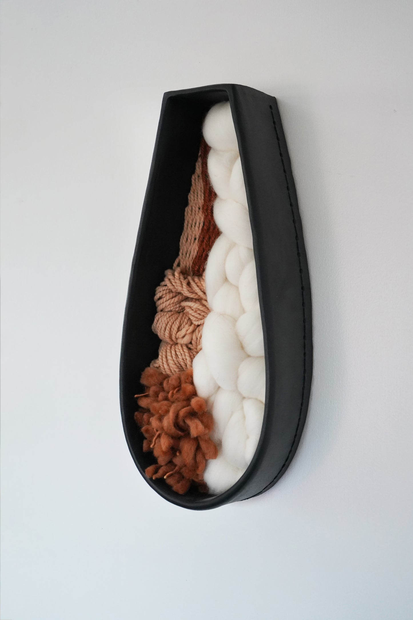 Side angle of the clay wall art highlighting the depth of the hand formed black clay vessel and the soft, plush fiber textures inside. Shows the three dimensional structure clearly.