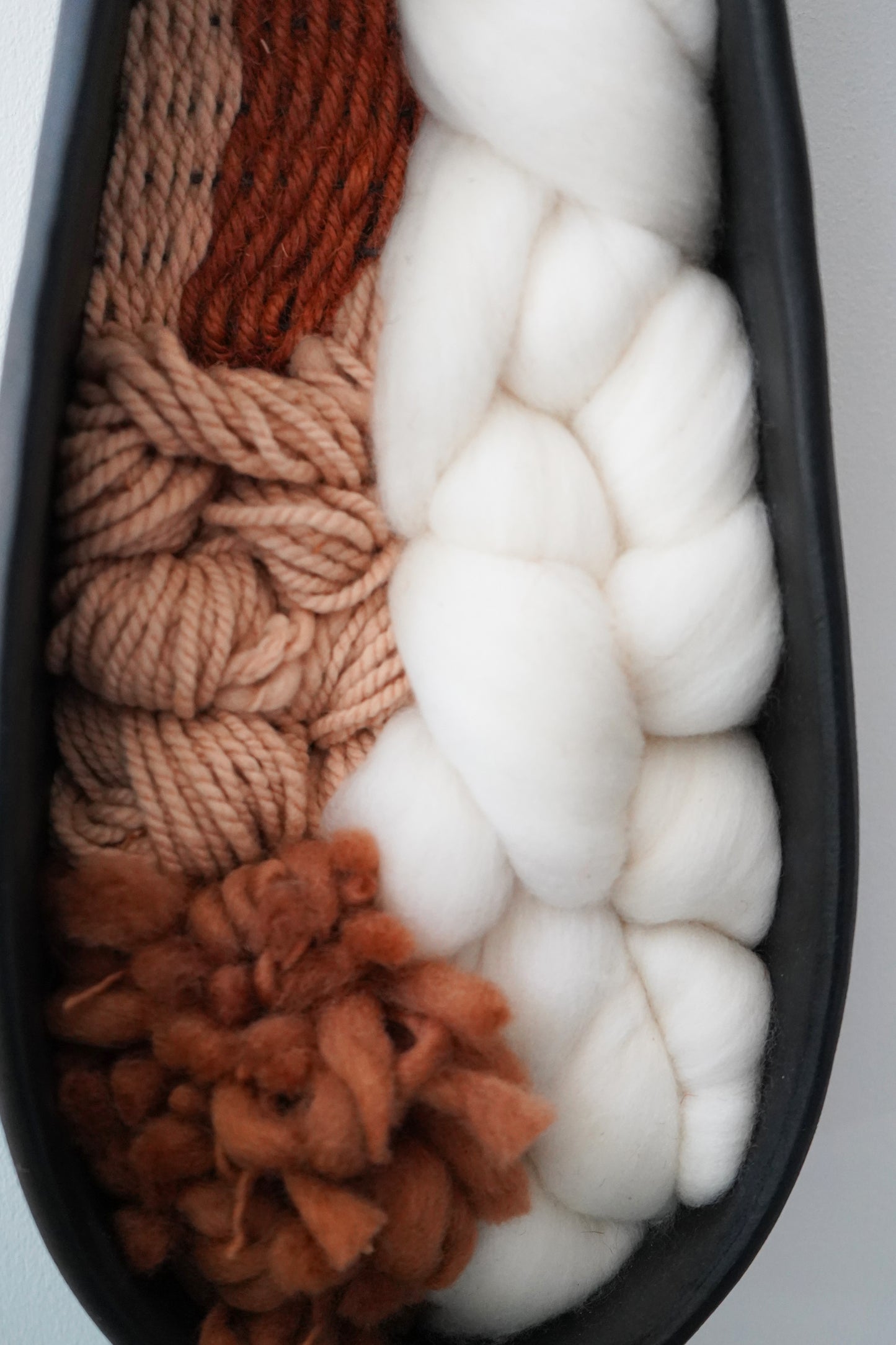 Close view of the woven interior showing textured Targhee wool, thick Rambouillet roving, and hand spun brown yarn inside a hand formed black clay frame. Detailed look at the natural fibers and organic texture by Keyaiira