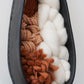 Close view of the woven interior showing textured Targhee wool, thick Rambouillet roving, and hand spun rust brown yarn inside a hand formed black clay frame. Detailed look at the natural fibers and organic texture.