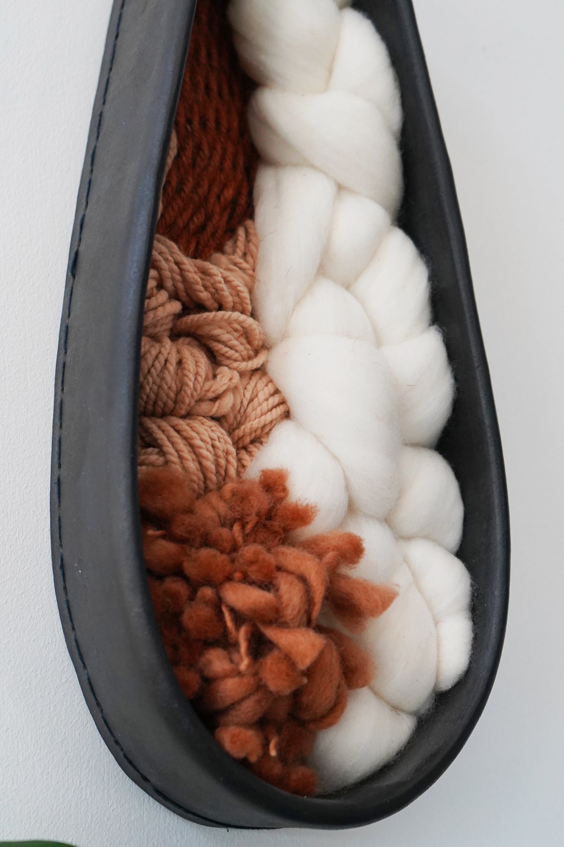Close view of the woven interior showing textured Targhee wool, thick Rambouillet roving, and hand spun rust brown yarn inside a hand formed black clay frame. Detailed look at the natural fibers and organic texture.