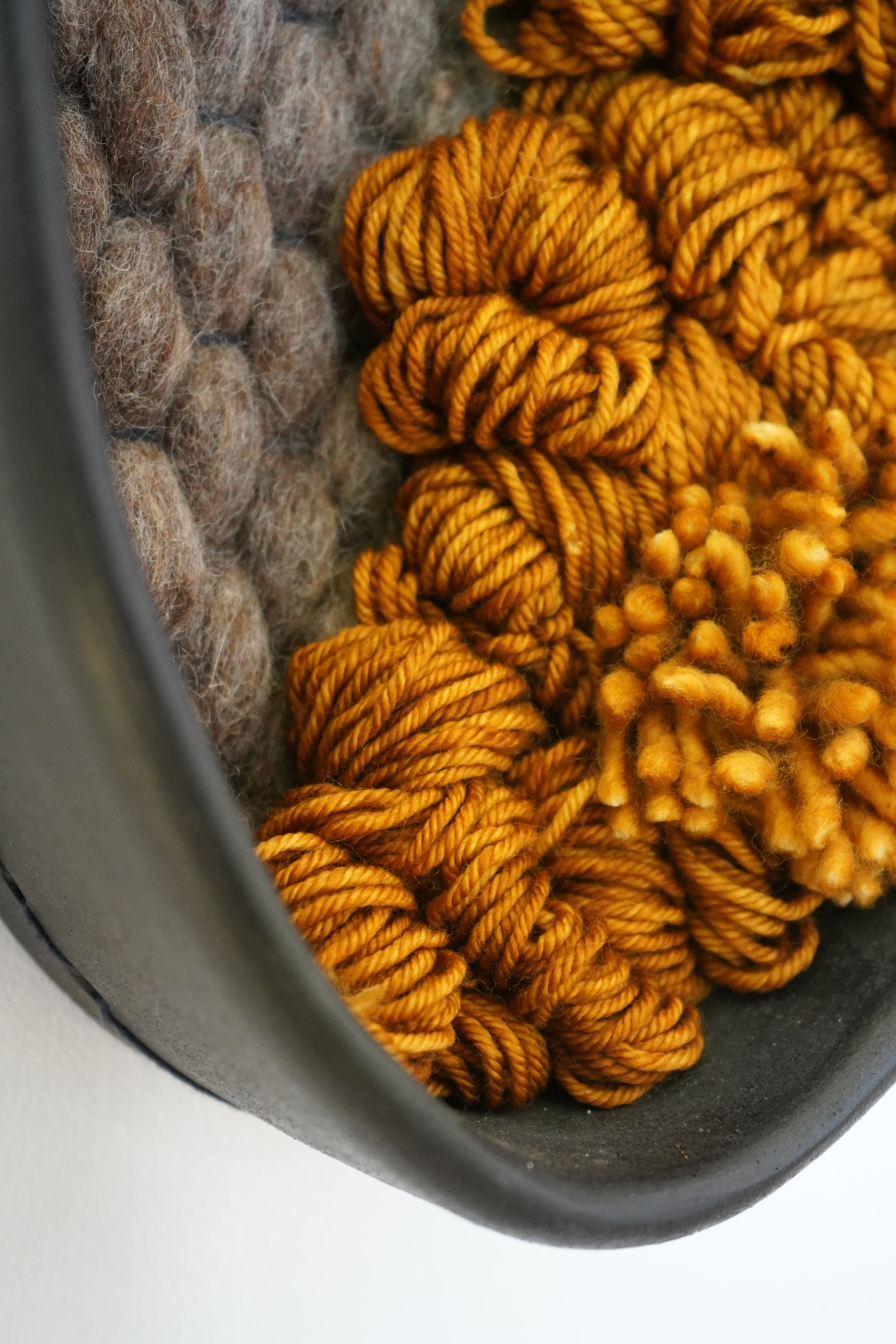 Close side view of handwoven wool artwork showing rich rusted orange texture inside black clay frame.