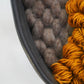 Detail close-up showing textural ochre wool loops against felted gray wool, highlighting fiber variation.