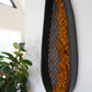 Interior design styling showing textural wool art next to fresh greenery. High-contrast black ceramic and mustard fiber wall hanging for residential or commercial projects.