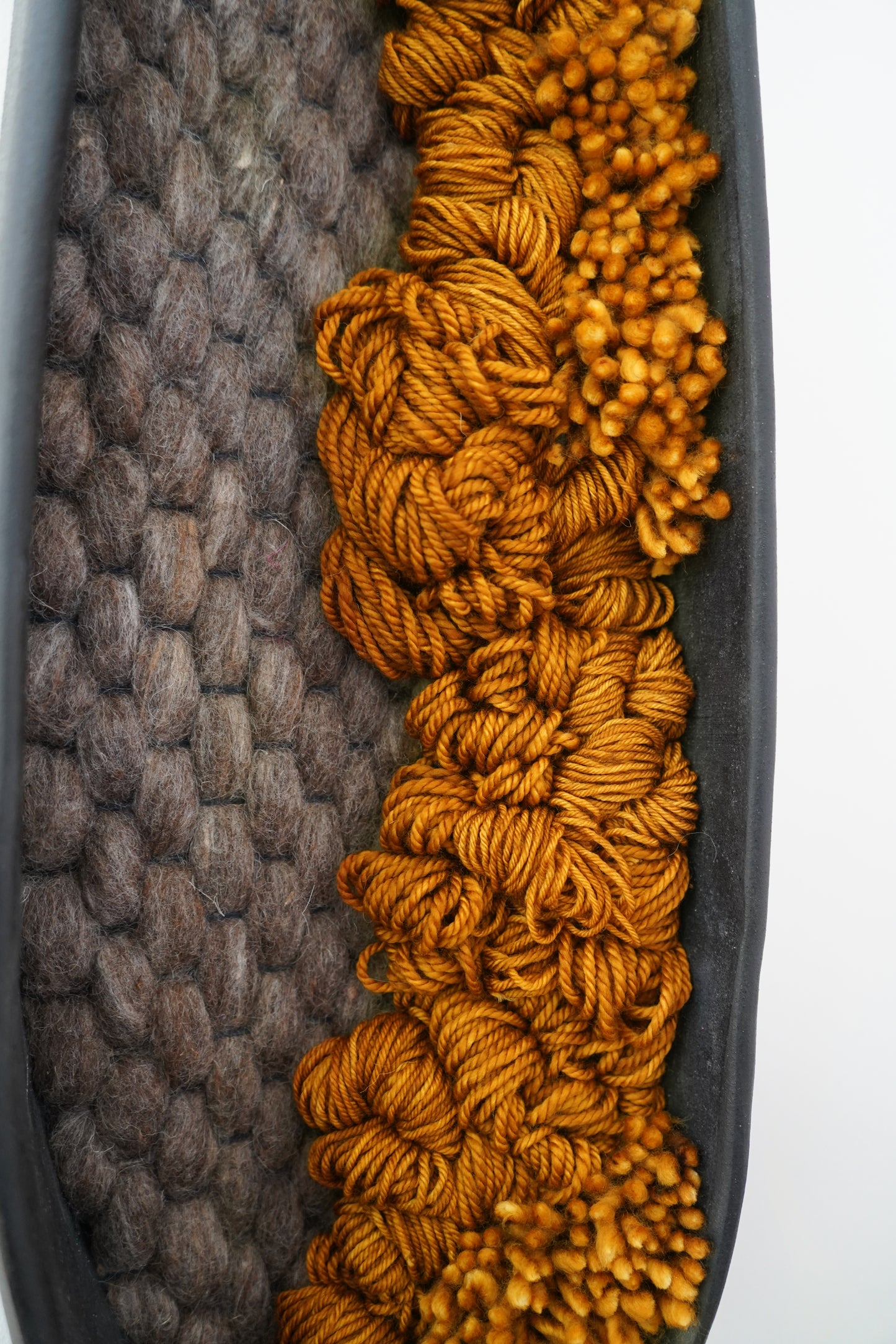 Vertical display of black clay fiber sculpture featuring rusted orange and gray wool, styled in organic modern interior.