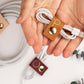 Thoughtfully designed leather cable wrap securing a white charging cord, hand-finished Keyaiira cord keeper with brass hardware for phone chargers, USB cables and everyday cable management

