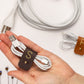 Personalized S initial leather cable keeper shown bundling white earbuds, a refined Keyaiira cord management accessory for headphones, charger wires and small electronics
