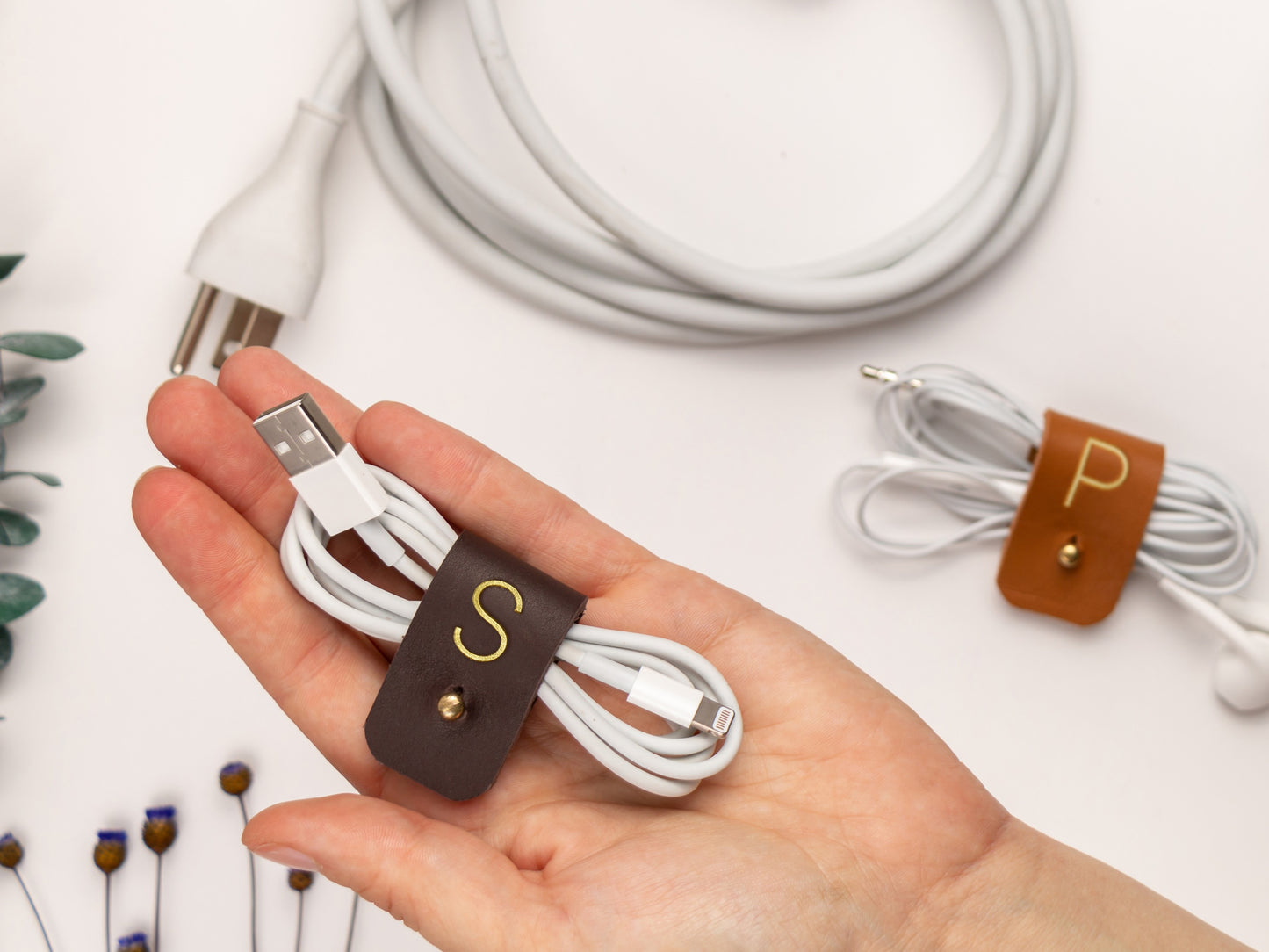 Personalized S initial leather cable keeper shown bundling white earbuds, a refined Keyaiira cord management accessory for headphones, charger wires and small electronics

