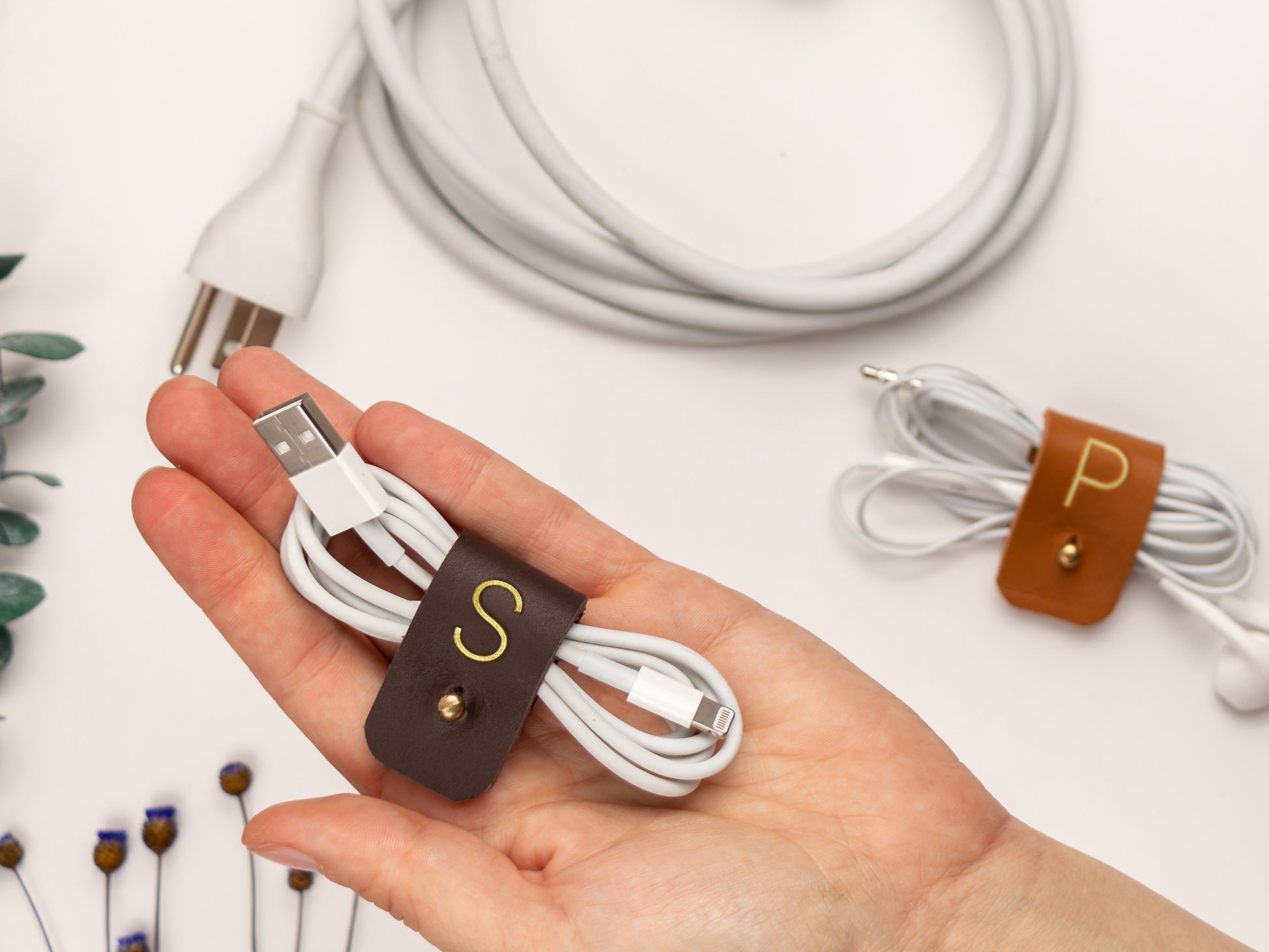 Personalized S initial leather cable keeper shown bundling white earbuds, a refined Keyaiira cord management accessory for headphones, charger wires and small electronics

