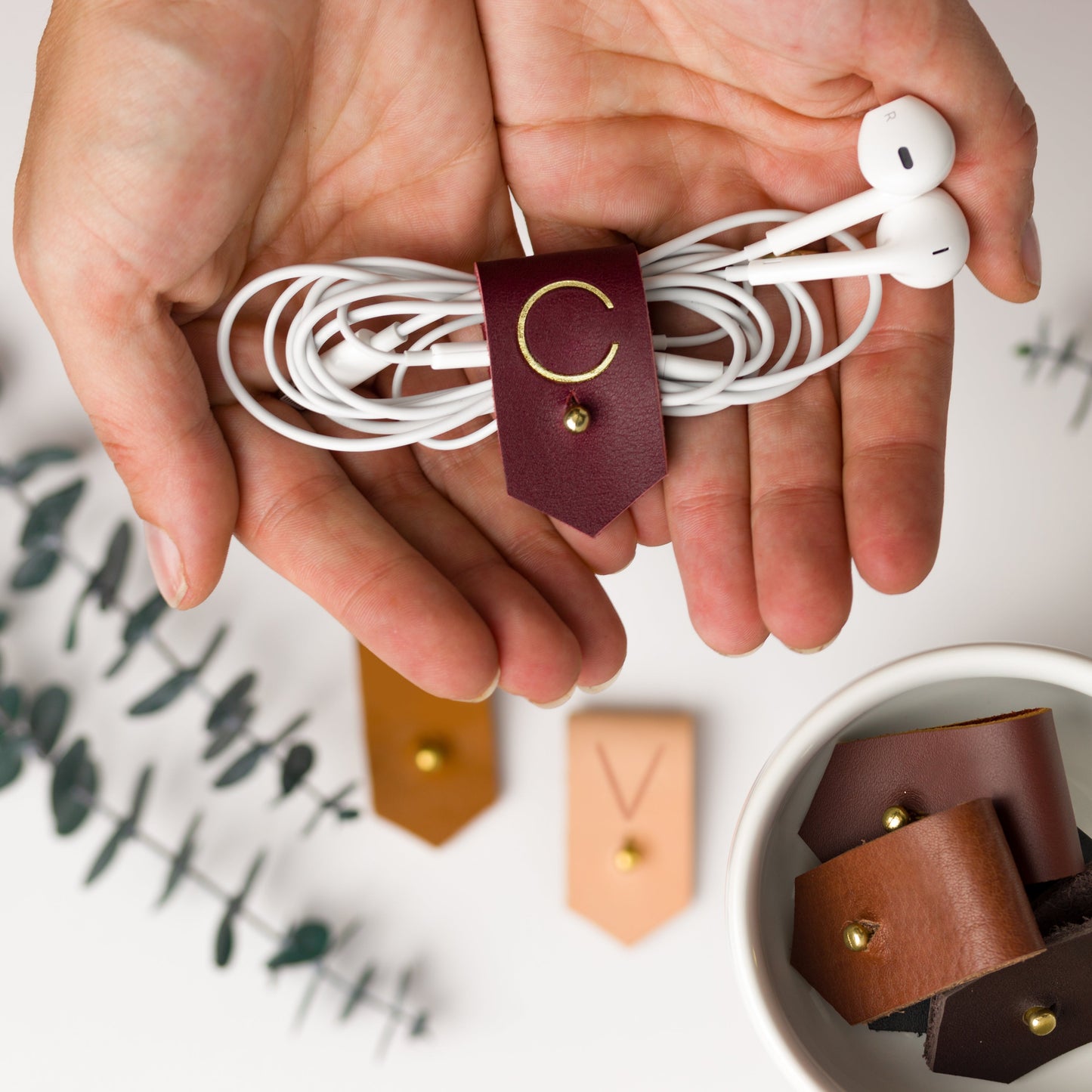 Wine full-grain leather earbud keeper with custom C initial, crafted by Keyaiira with minimal brass stud & post hardware for wired headphones, small cords and tangle-free everyday storage
