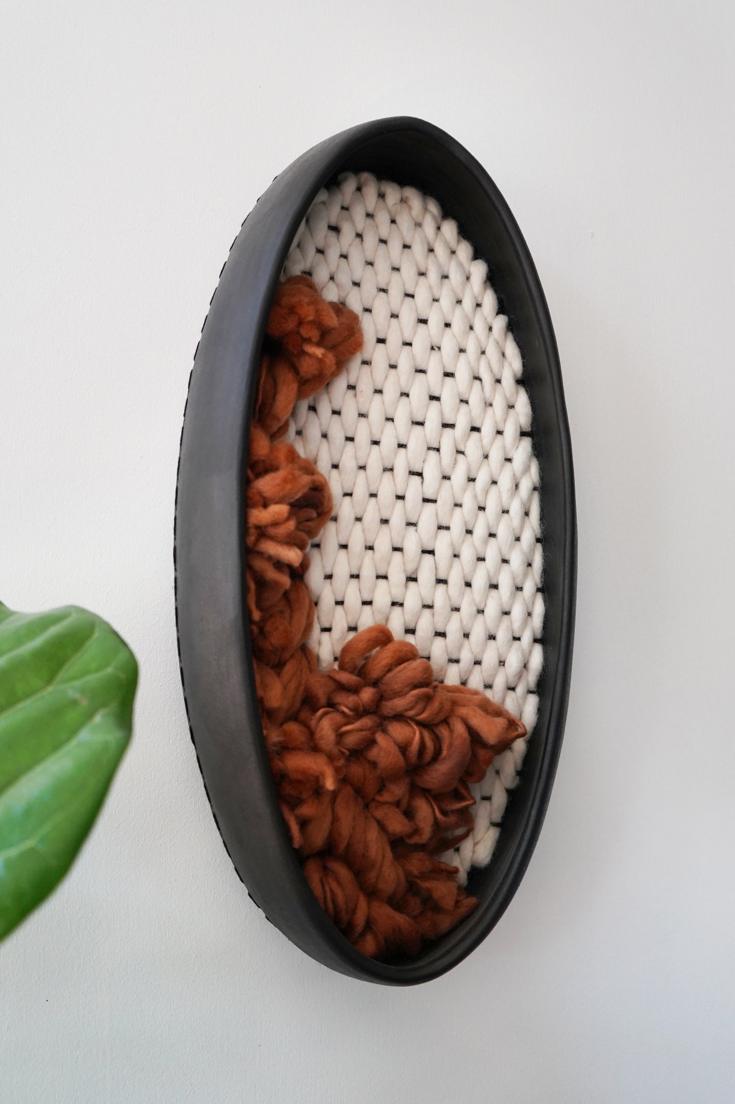 Collaborative fiber art wall sculpture by Keyaiira. Features a hand-formed black clay frame by Sonoma artist Kala Stein and sustainable New Zealand wool felted in Nepal. A unique blend of ceramic and textile craftsmanship.