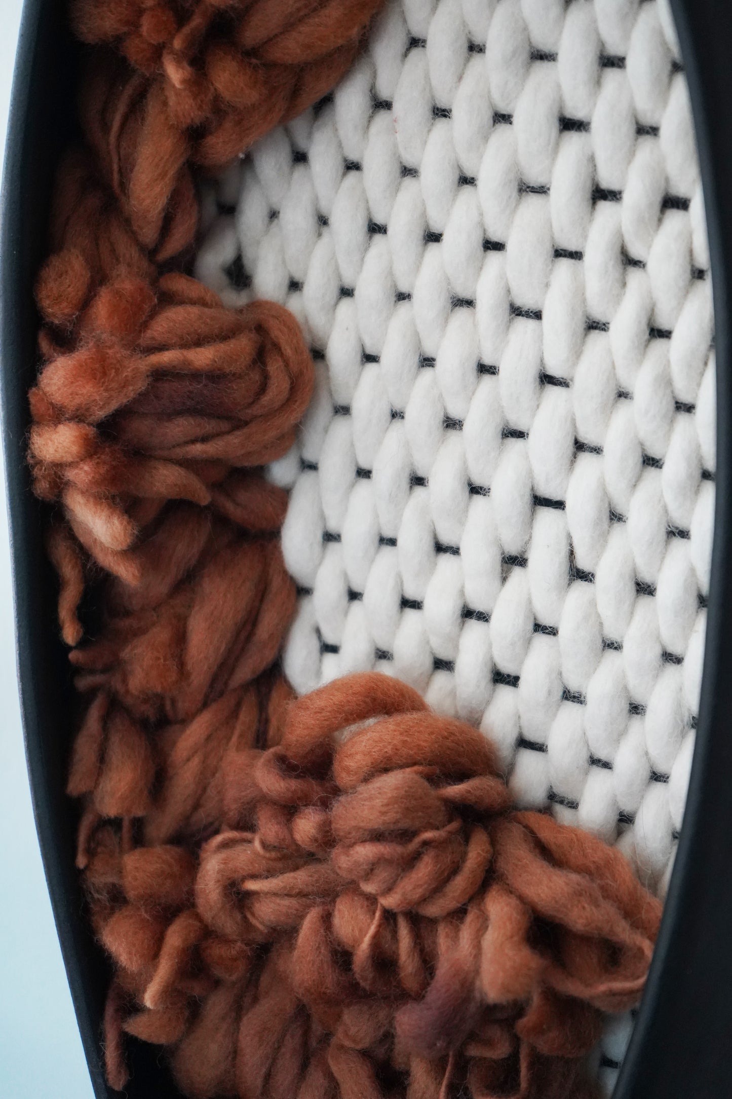 Sustainable wall decor made from ethically sourced materials. Matte black ceramic vessel filled with hand-dyed rust wool yarn and ivory hand-felted fibers. Sourced from small woman-owned businesses in Northern California.