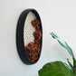 Handcrafted matte black ceramic clay frame wall sculpture sized 19x9.5 inches. The interior features a woven ivory wool grid with organic, rust-brown thick and thin wool yarn cascading from the center. Modern bohemian fiber art by Keyaiira.