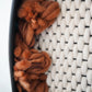 Macro detail of Zenia wall sculpture texture. Hand-spun rust thick-and-thin wool yarn loops emerge from a hand-felted ivory New Zealand wool grid, framed by a sleek matte black ceramic clay rim.