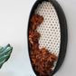 Side angle of black clay wall hanging showing the 3.25-inch depth of the ceramic frame. Demonstrates the dimensional quality of the fiber art where the rust wool emerges from the flat ivory woven base