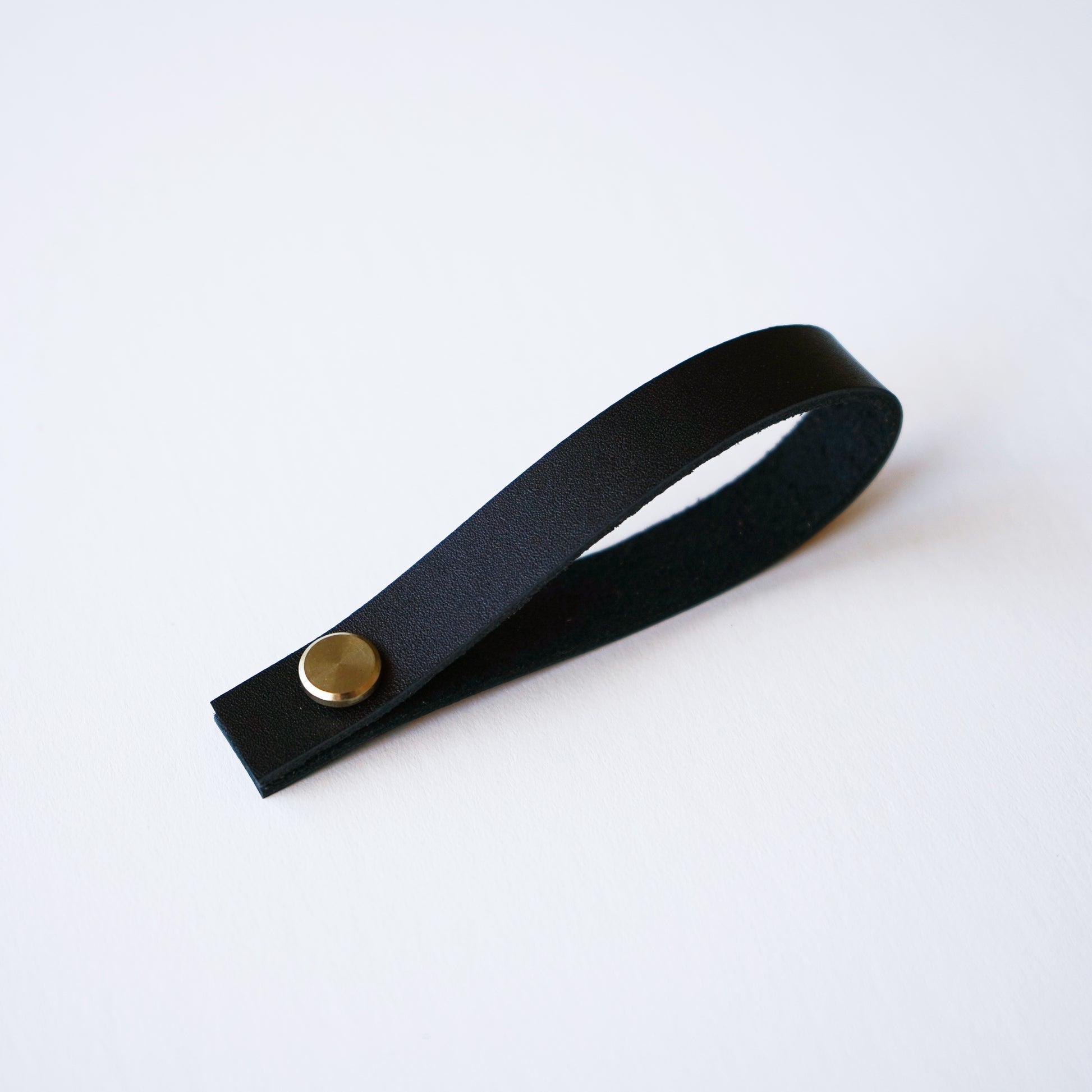 Black leather hanging loop with brass rivet on white background — handcrafted removable leather loop by Keyaiira.