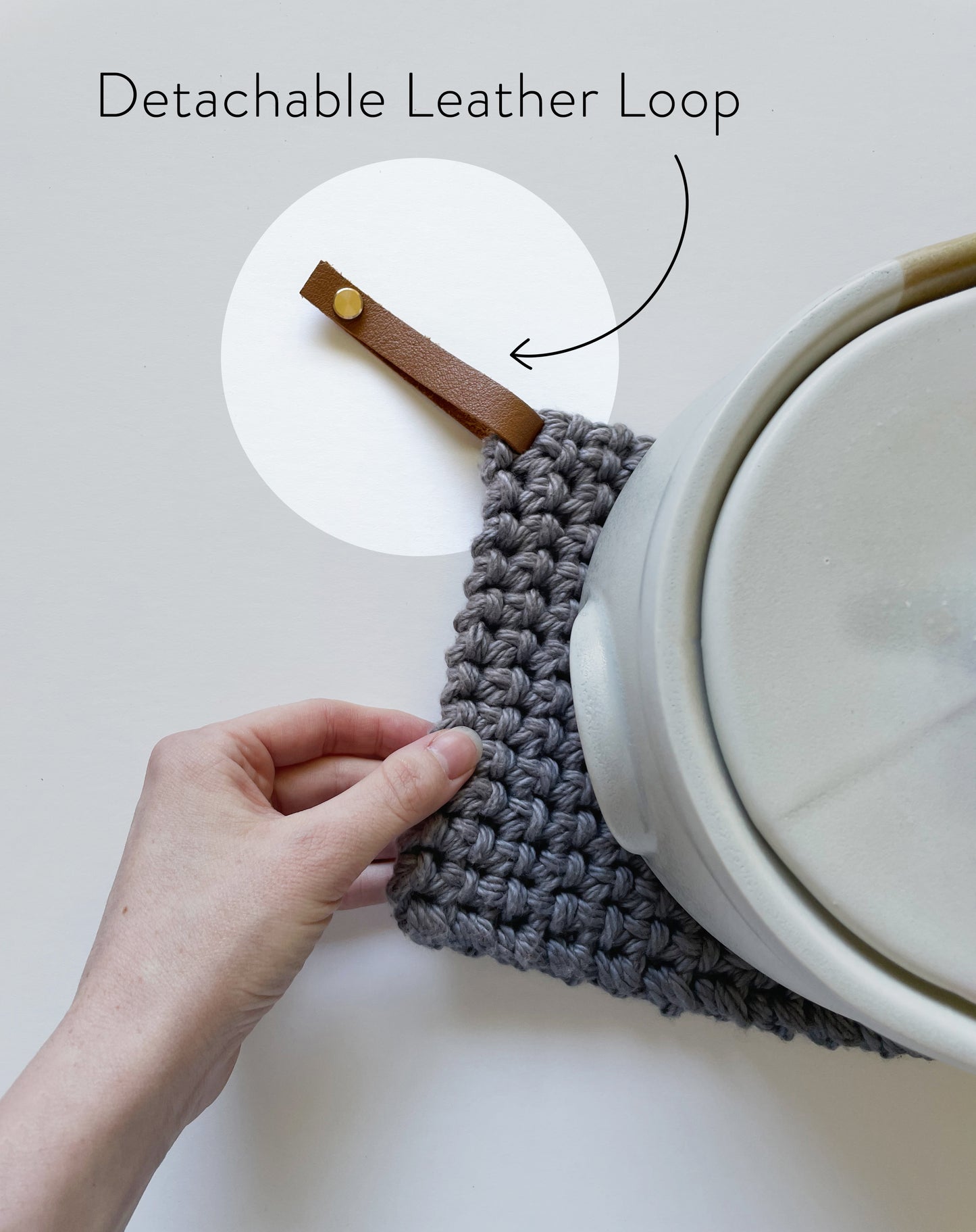 Hand holding a knit potholder with a detachable leather hanging loop attached Keyaiira handcrafted leather loop accessory.
