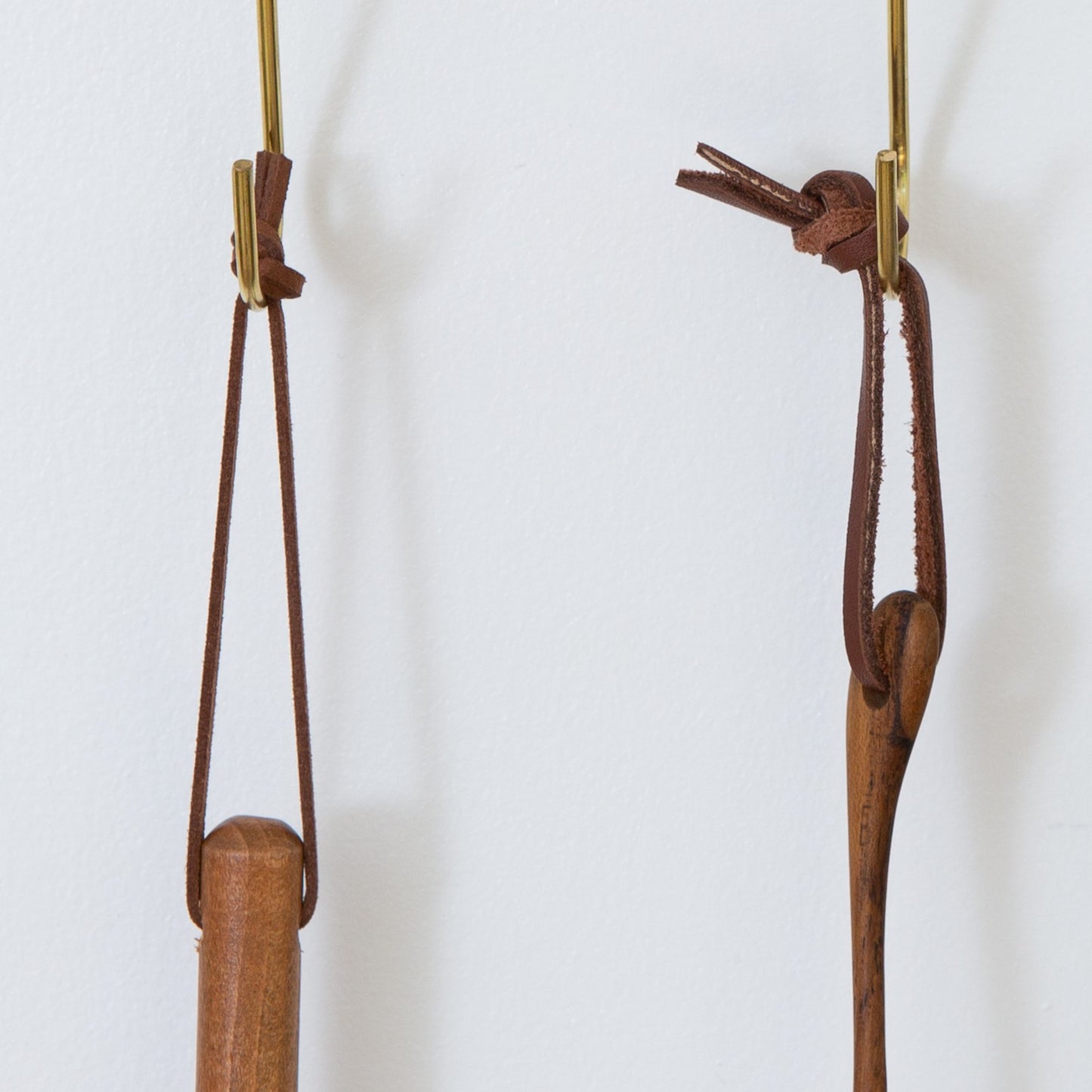 Two sets of detachable leather hanging strings by Keyaiira suspended from wall hooks — handcrafted leather hanging strings for minimalist home and kitchen organization with a white wall behind. 