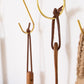 Multiple detachable leather hanging strings by Keyaiira displayed on brass wall hooks — handmade leather hanging strings for hanging kitchen tools and textiles.