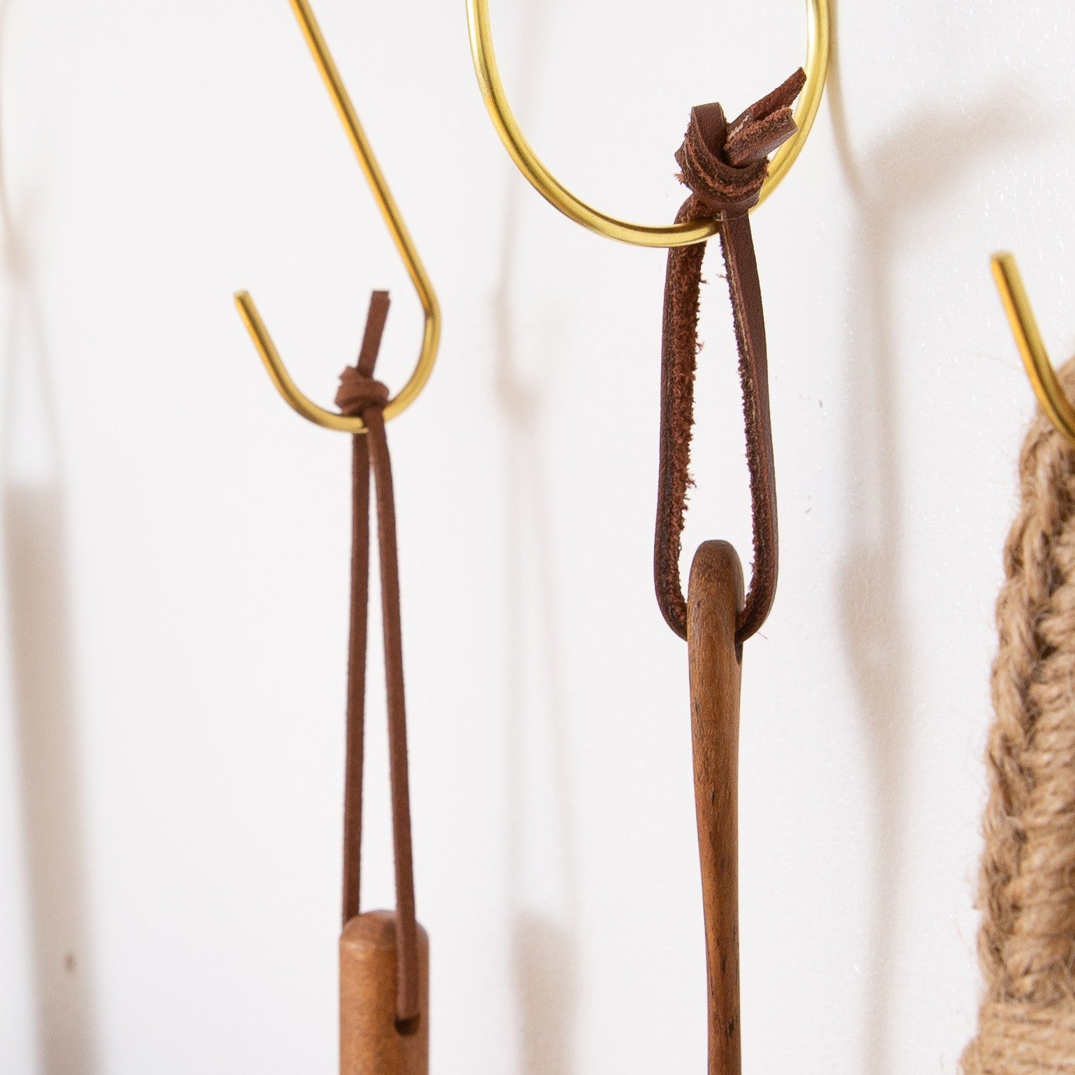 Multiple detachable leather hanging strings by Keyaiira displayed on brass wall hooks — handmade leather hanging strings for hanging kitchen tools and textiles.